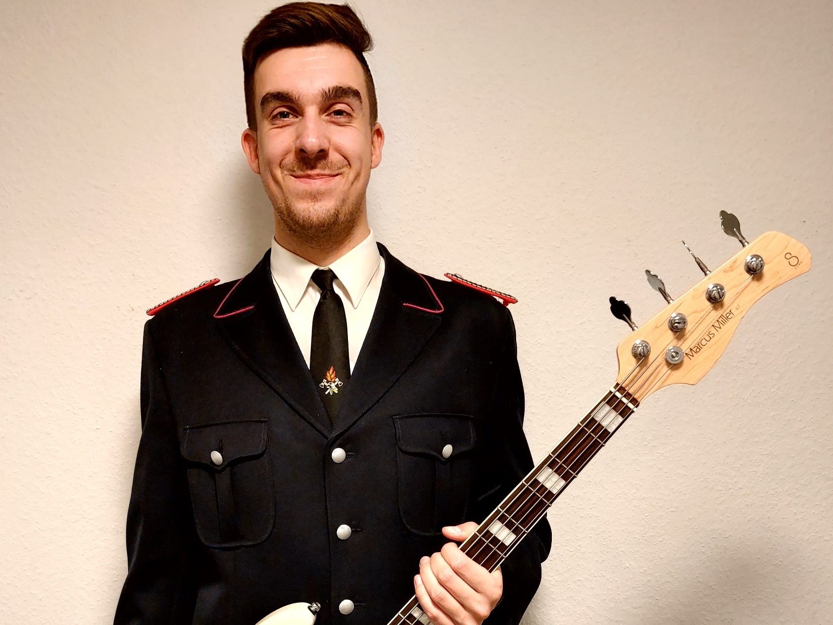 Tom in Feuerwehr-Uniform lächelt in die Kamera und hält eine Bassgitarre